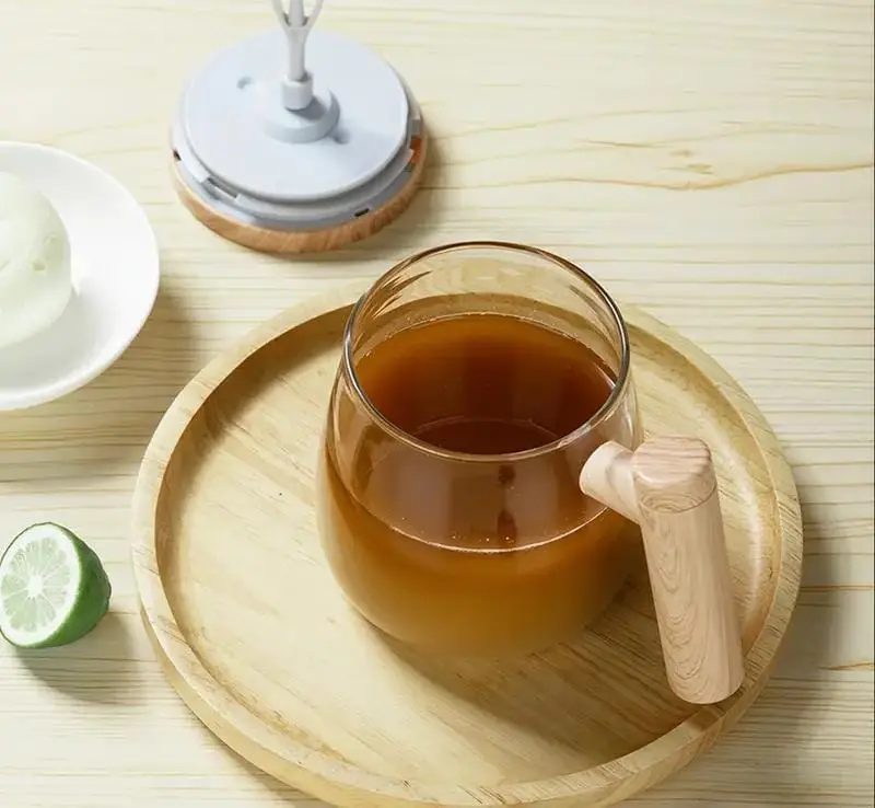 Taza mezcladora eléctrica con asa de madera y bebida marrón sobre bandeja de madera.