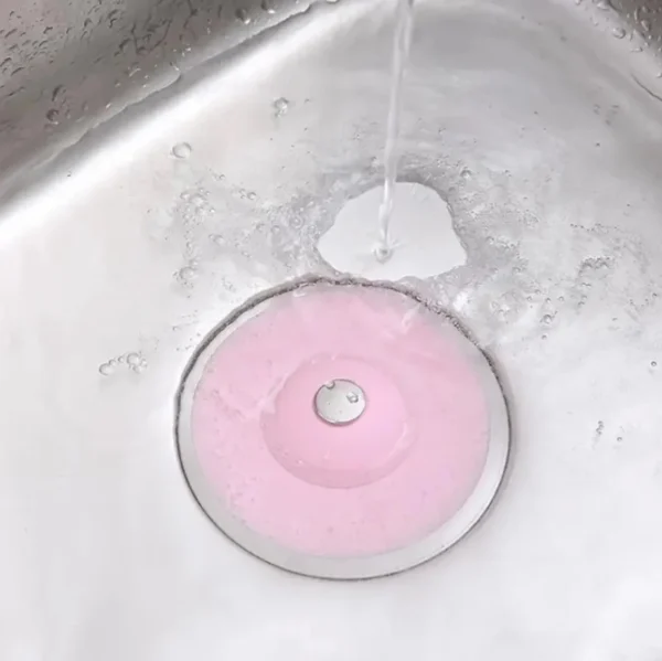 Tapón de silicona rosa para desagüe de lavaplatos con agua cayendo.