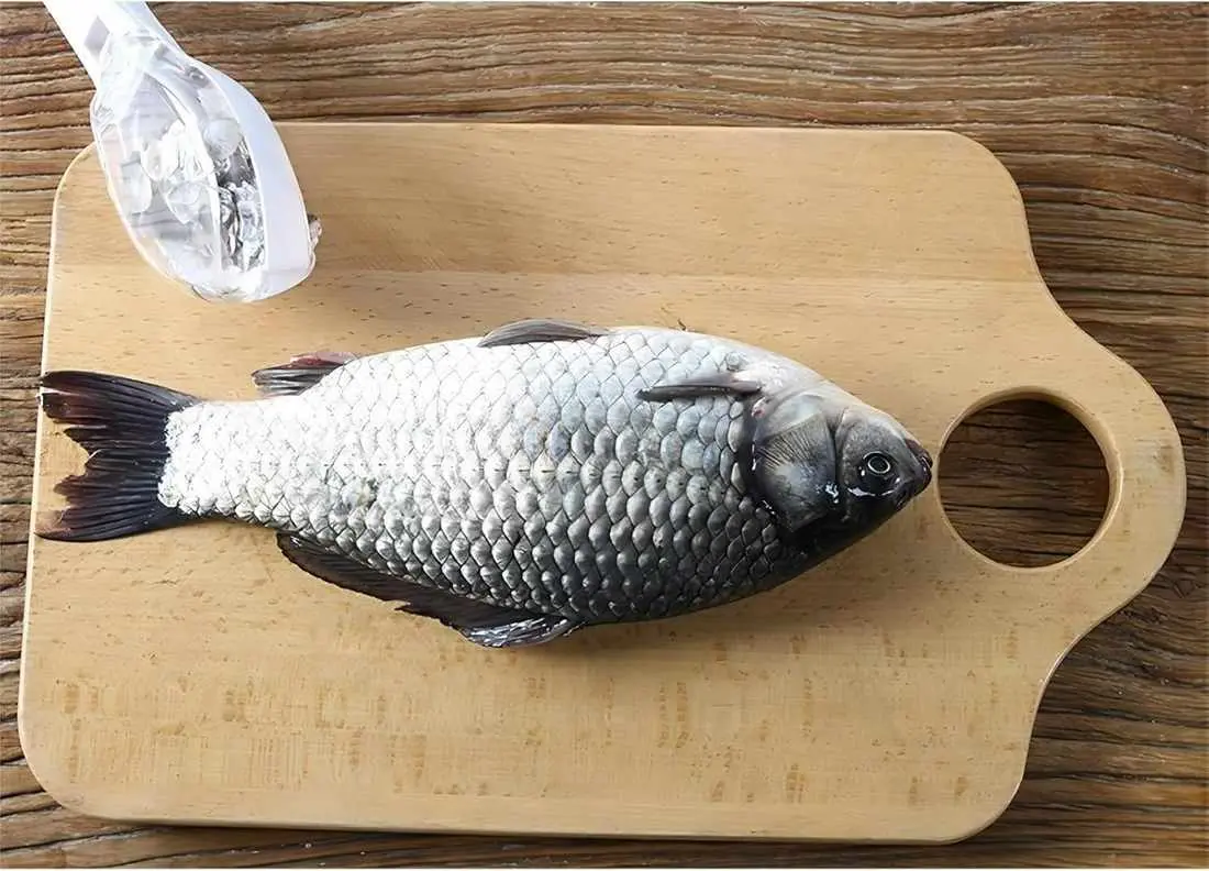 Set x2 limpiador de escamas de pescado sobre tabla de madera, con pez fresco listo para limpiar.