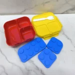 Mini Coca Lonchera para Niños Tipo Lego con compartimentos en rojo y amarillo, accesorios azules.