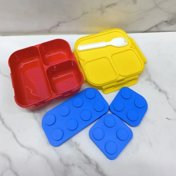 Mini Coca Lonchera para Niños Tipo Lego con compartimentos en rojo y amarillo, accesorios azules.