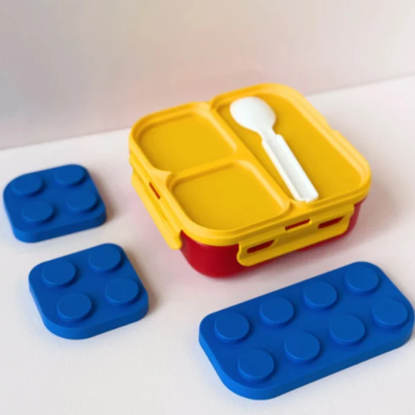 Lonchera Coca-Cola tipo Lego, roja y amarilla, con tres bloques Lego azules, ideal para niños.