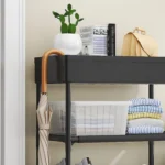 Estante zapatero multiusos negro con cactus, paraguas, libros, bolso y ropa organizada.