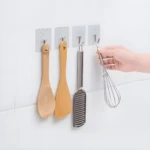 Cepillos de madera y batidor colgados en ganchos adhesivos en pared blanca.