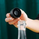 Apon Bomba para Vino Sellador Tapa con S en mano, cerca de botella de vidrio.