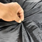 Mano sujetando carpa pijama para moto negra con logo de marca visible.