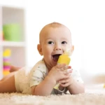 Bebé feliz jugando con cuchara biberón de papillas amarillas, ideal para lactantes.