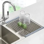 Escurridor enrollable para platos de acero inoxidable sobre el lavaplatos con vasos y limones.