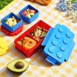 Fiambrera lonchera Lego azul con compartimentos llenos de comida para picnic.