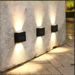 Lámparas solares de aplique LED que iluminan pared de concreto y camino de ladrillo.