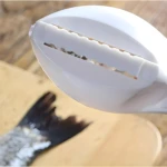 Set x2 limpiador de escamas de pescado blanco en acción sobre un pez en tabla de madera.