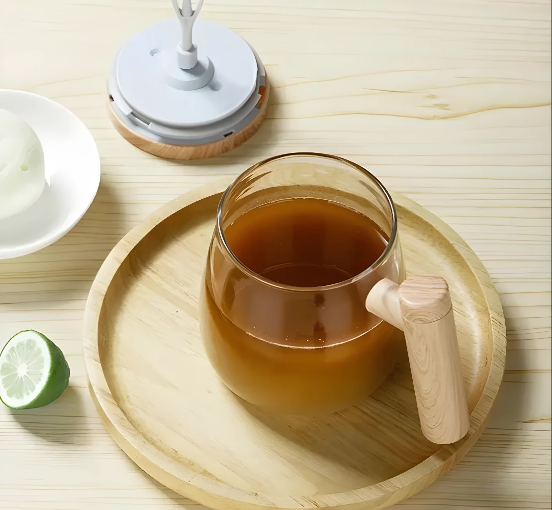 Taza mezcladora eléctrica con bebida marrón y rodaja de limón en bandeja de madera.