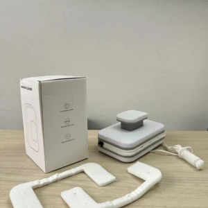 Limpia vidrios magnético doble cara con almohadillas blancas y cuerda de seguridad en mesa de madera.