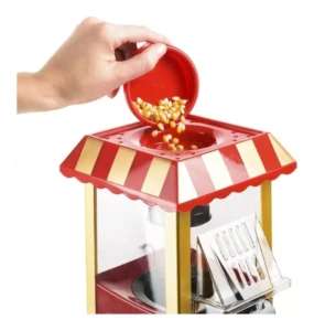 Máquina crispetera eléctrica agregando maíz a la parte superior, diseño rojo y dorado.