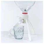 Soporte dispensador para botellón con grifo y vaso de vidrio, ideal para agua.