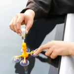 Kit reparador de vidrio automotriz para grietas, manos aplicando resina con ventosas.