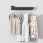 Tendedero plegable de pared con tres vestidos colgados: beige, blanco y estampado de lunares.