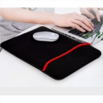 Funda para portátil de neopreno negra con borde rojo, con mouse y manos escribiendo.