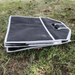 Organizador para carro o camping plegable negro con asas, sobre pasto.