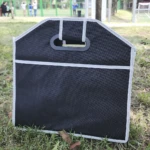 Organizador negro para carro o camping, con asas y borde blanco, al aire libre.