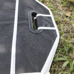 Organizador negro para carro o camping con asa de plástico, sobre pasto y tierra.