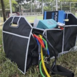 Organizador de carro y camping negro plegable con bandas de resistencia y objetos varios.