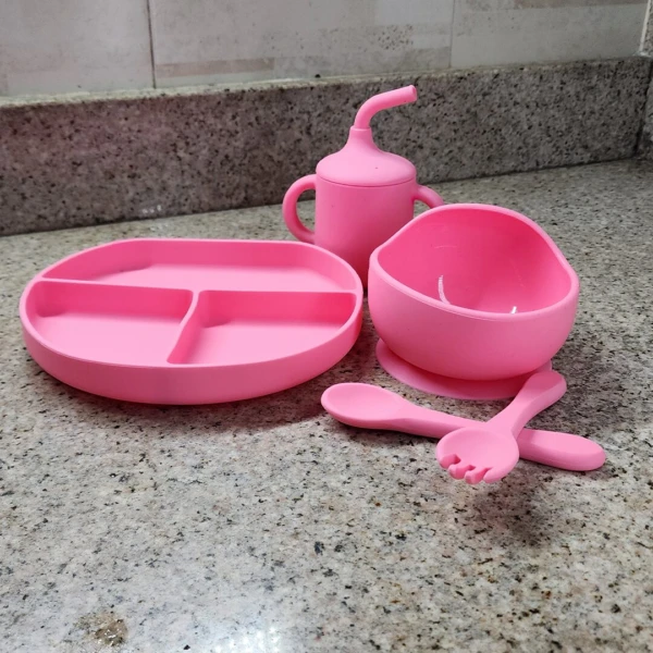 Vajilla de silicona para bebé rosa: plato con divisiones, tazón con ventosa, vaso y cubiertos.