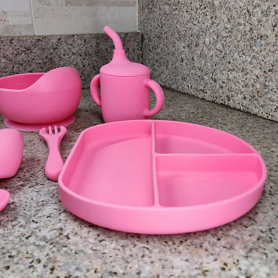 Vajilla de silicona para bebé en color rosa: plato con divisiones, vaso con popote, tazón y cubiertos.