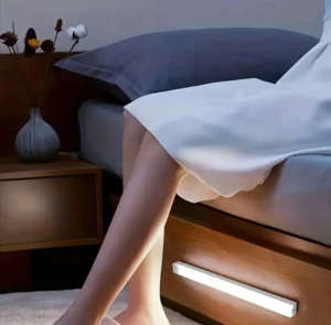 Barra de luz inalámbrica recargable debajo de la cama ilumina suavemente las piernas de una persona.