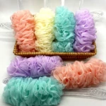 Cepillos corporales para ducha con esponjas de colores pastel en canasta y sobre superficie blanca.