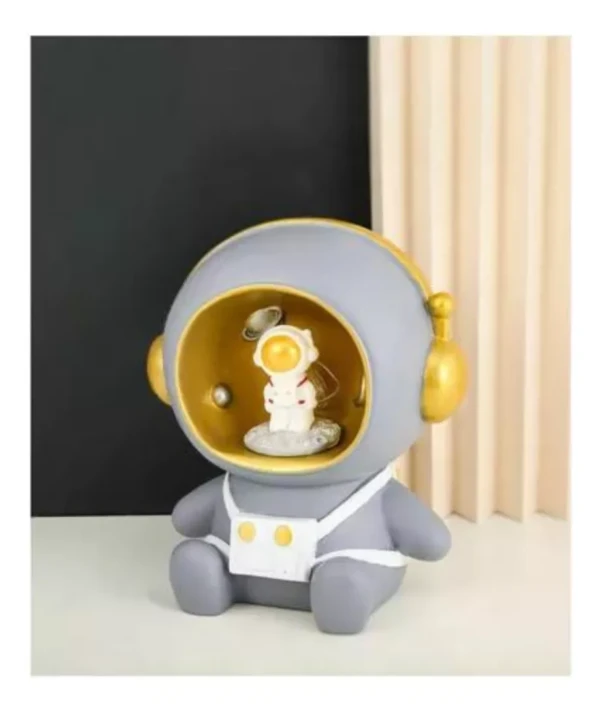 Lámpara alcancía de astronauta sentado, con figura espacial y detalles dorados.