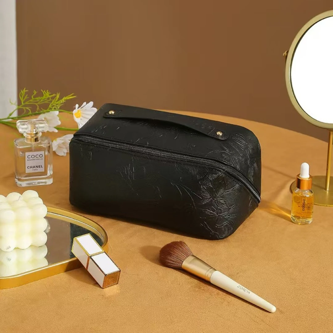 Cosmetiquera negra texturizada con compartimentos, set de maquillaje y espejo de tocador.