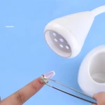 Lámpara UV LED profesional para uñas con pinza aplicando un diseño de pedrería.