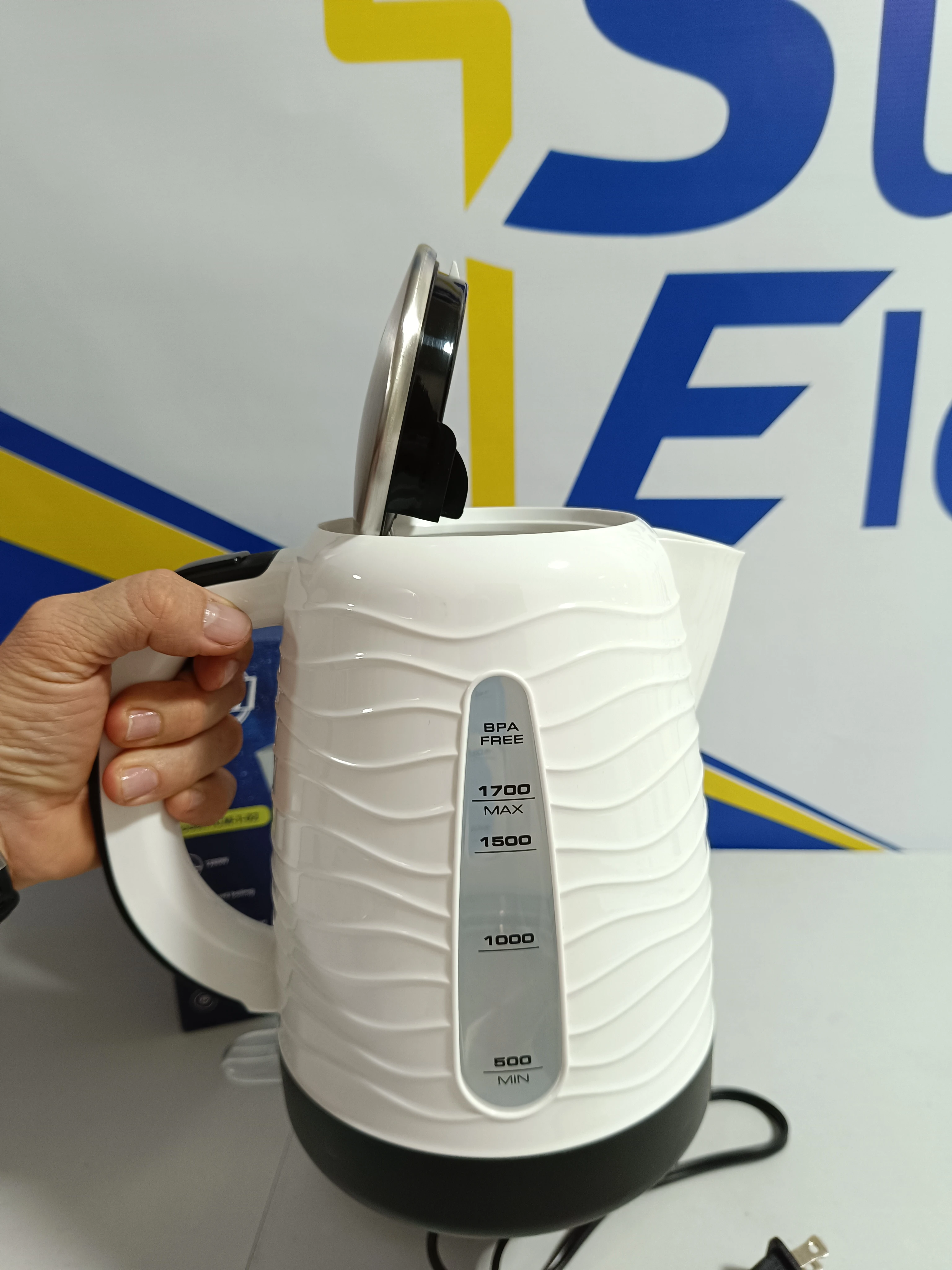 Tetera hervidor de agua blanca 1.7L ICM con medidor, tapa abierta y mano sujetando el asa.
