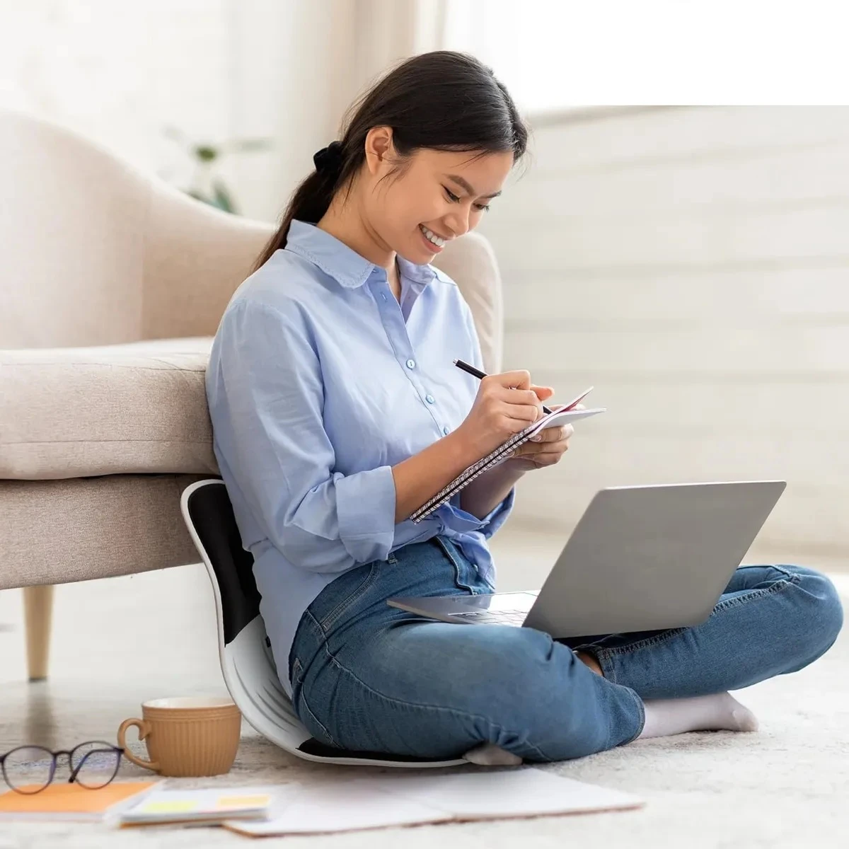 Espaldar corrector de postura para silla, joven escribiendo en cuaderno y laptop en el suelo.