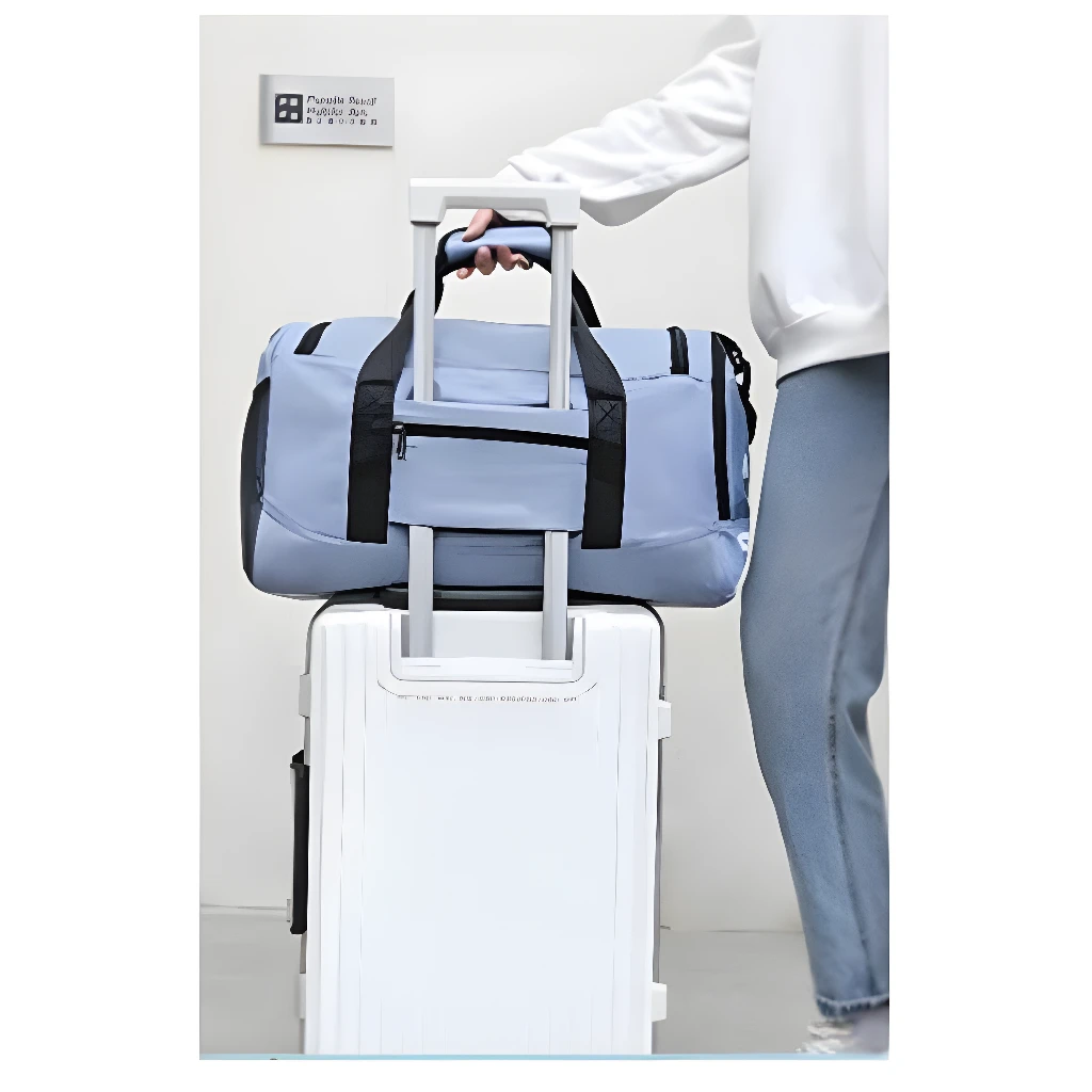 Bolso grande de viaje azul claro apilado sobre una maleta blanca con asa extensible.