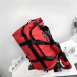 Bolso viajero multiuso rojo con correas negras y logo visible.