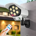 Cámara falsa con lámpara solar de movimiento y control remoto en pared de ladrillo.