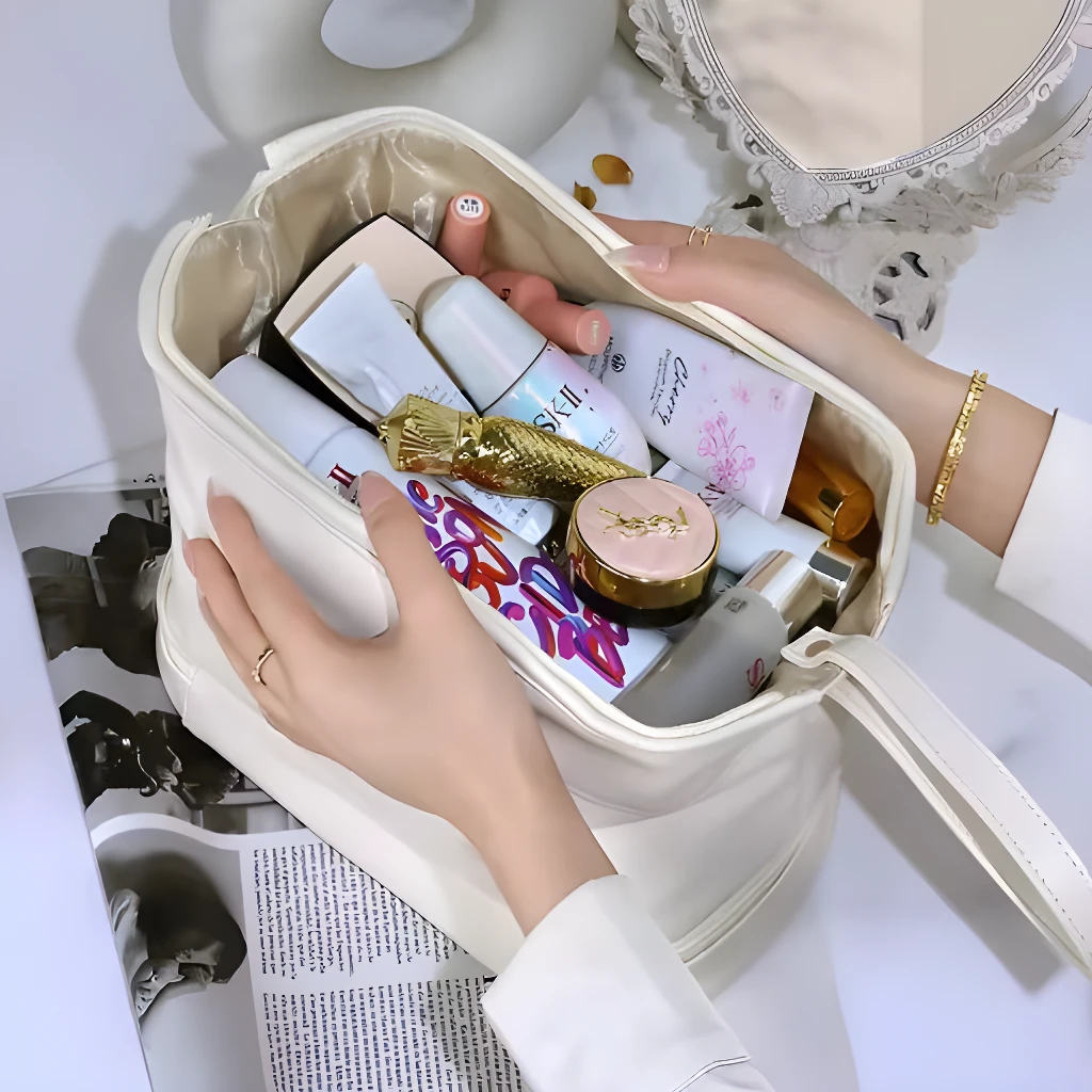 Cosmetiquera beige de doble compartimiento con productos de belleza y manos arregladas.
