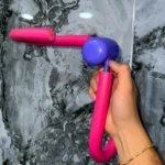 Ejercitador de pierna multiusos rosa y morado en mano sobre fondo de mármol gris.