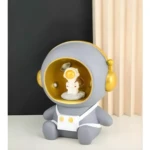 Lámpara Alcancía astronauta gris con detalles dorados, figura espacial.