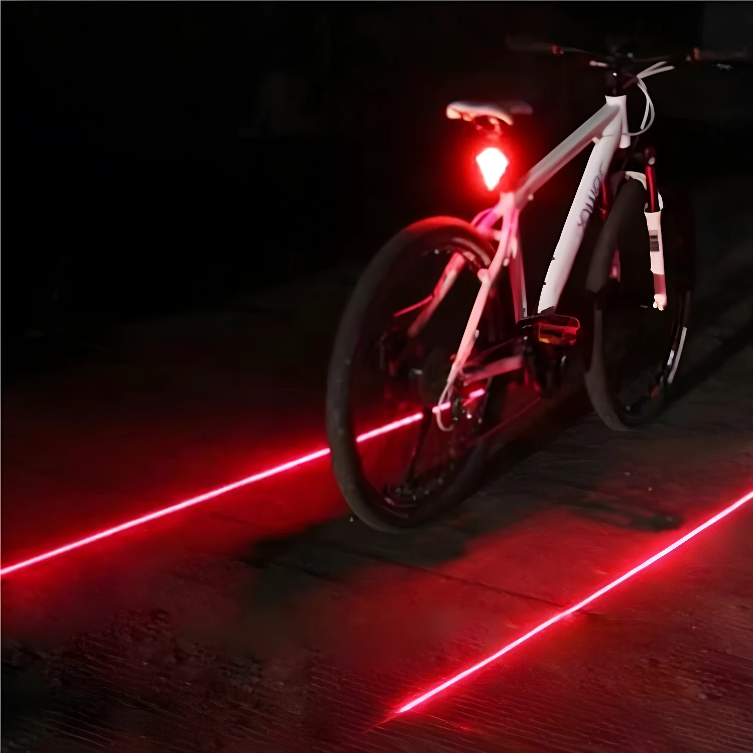 Luz roja de bicicleta proyecta carriles láser en el suelo oscuro.