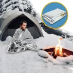 Manta térmica de emergencia para temperaturas extremas, hombre abrigado en carpa nevada junto a fogata.