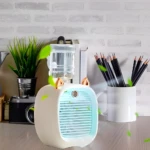 Mini ventilador refrigerador recargable blanco con orejas doradas, en escritorio con planta y lápices.