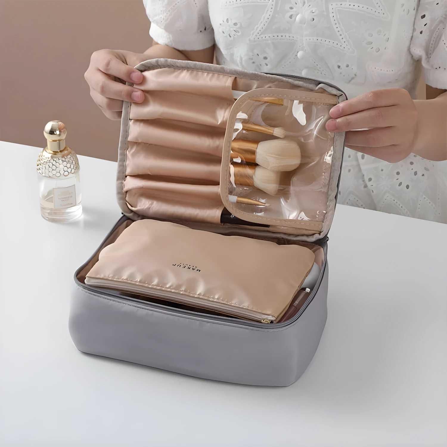 Neceser organizador de maquillaje de viaje gris con compartimentos y pinceles visibles.