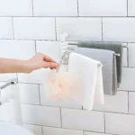 Organizador de toallas giratorio plateado para baño, colgado en azulejos blancos.