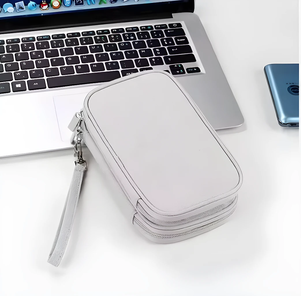 Estuche gris para organizar baterías y cables, con correa de mano y cremallera, junto a un portátil.