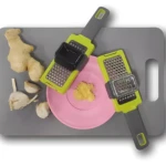 Rallador de ajo con jengibre y ajos sobre tabla gris.