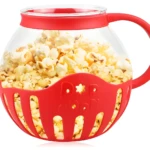 Recipiente de vidrio para crispetas con tapa y base roja, lleno de crispetas recién hechas.