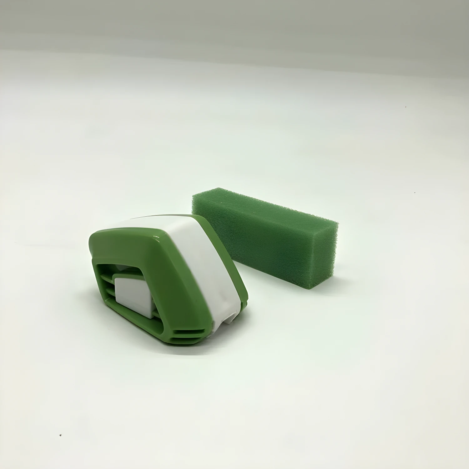 Reparador de plumilla verde y blanco junto a bloque de esponja verde sobre fondo blanco.